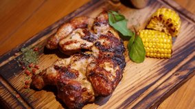 Stock food video of chicken hips cooked on grill in American meat restaurant and served on rustic wooden plate with corn. Poultry hip grilled for dinner