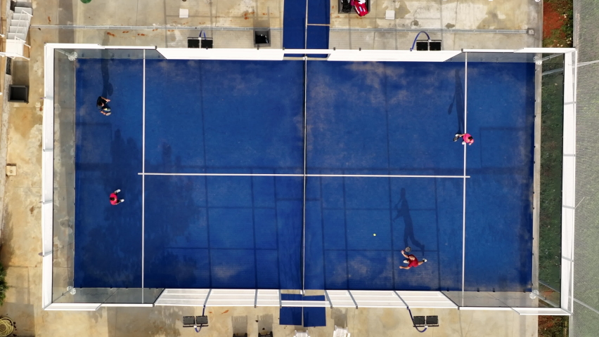 View from above, aerial footage, slow motion video of some people playing on a blue padel court. Padel is a mix between Tennis and Squash. It's usually played in doubles on an enclosed court. Royalty-Free Stock Footage #1082477881