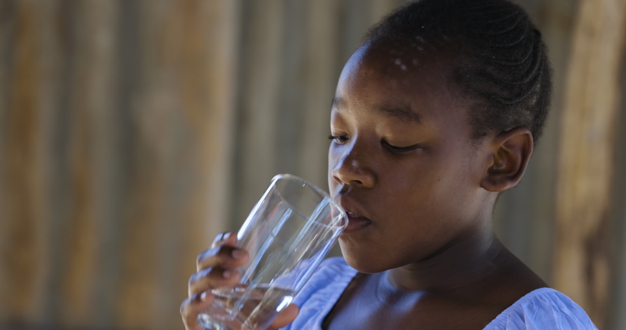 Poverty.Inequality.Cute young Black African girl drinking water from a glass in a township