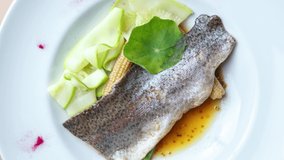 Stock food video of sea bass fish for lunch in seafood restaurant. Gourmet seabass served on white plate, filmed from above on table