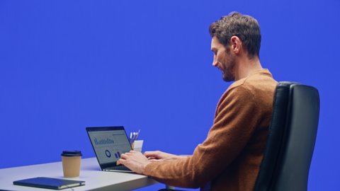 Green Screen Office Background: Caucasian Businessman Sitting at His Desk Working on a Laptop Computer. White Man working with Big Data e-Commerce Analysis. 360 Degree Tracking Shot. Moving Around