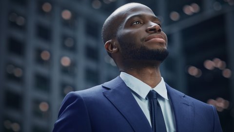 Portrait of Successful Stylish Black Businessman in Suit, Standing on the Big City Street, Looking Afar, Then Turning Down to Look at the Camera. African American Entrepreneur. Slow Motion Low Angle