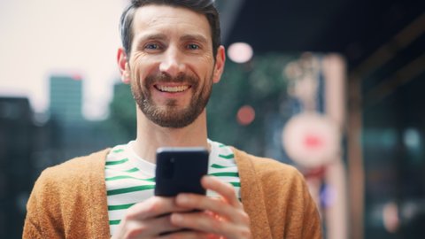 Portrait of Caucasian Man Using Smartphone, Looking at Camera, Having Fun in Big City. Creative Male Using Mobile Phone App for e-Commerce Investment, Online Shopping, Social Media, Internet Browsing