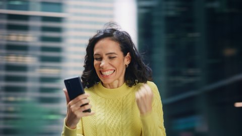360 Degree Street Shot: Portrait of Beautiful Latin Woman Using Smartphone, Celebrating Successful Victory. Smiling Hispanic Female Entrepreneur Using Mobile Phone Happily. Tracking Moving Around Shot
