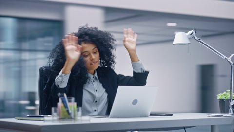 360 Degree Office: Black Businesswoman Dances and Smiles While Sitting at Her Desk. Beautiful Female Specialist Works on Laptop Celebrates Successful e-Commerce Project. Tracking Moving Around Shot