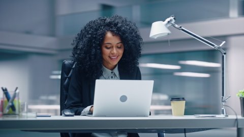 360 Degree Office: Black Businesswoman Sitting at Her Desk Working on a Laptop Computer. Smiling Successful African American Woman working with Big Data e-Commerce. Moving Around Tracking Shot