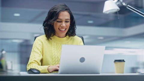 360 Degree Office: Happy Smiling Hispanic Businesswoman Sitting at Her Desk Working on a Laptop Computer Celebrates Victory. Latin Female Entrepreneur is a Happy Winner. Hands to Face Tracking Shot