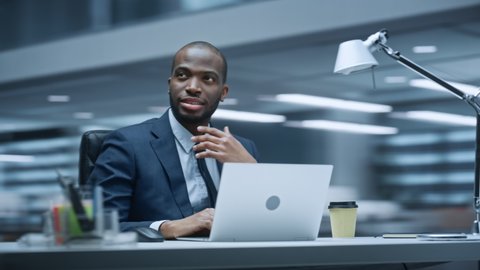 360 Degree Office: Handsome Successful Black Businessman Sitting at Desk Using Laptop Computer. African American Entrepreneur in Suit working with Stock Market Investing. Moving Around Tracking Shot