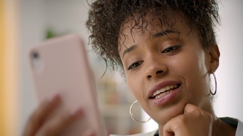 Close up of Happy African American Young Woman Using Smartphone Working or Studying From Home. Video Conference Call at Home Office. Friends Chatting, Online Learning or Teleworking Concept.