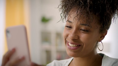 Close up of Happy African American Young Woman Using Smartphone Waving and Laughing. Video Conference Call at Home Office. Friends Chatting, Online Learning or Teleworking Concept.
