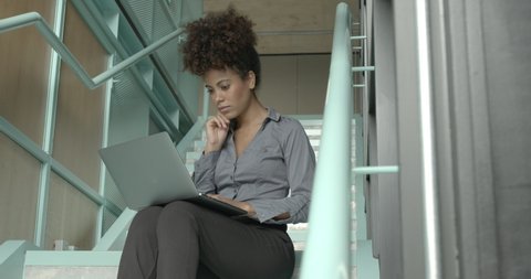 Business woman working in office on staircase on laptop