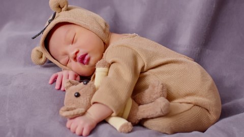happy newborn baby weaing cute Mouse costume lying sleeps and hug doll on Beige background comfortable and safety.Cute Asian infant sleeping and napping on baby bed.Newborn Baby photography concept