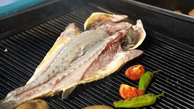 Cooking barbecue sea bass fish on grill. Roasting seafood with vegetables. 4k video.