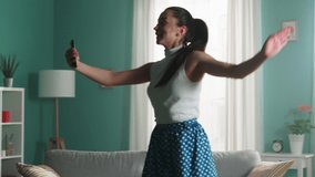 Young brunette woman in green skirt and white top is having great time at home, streaming positive video using smartphone, dancing and smiling, sharing positive mood with her followers, Slow motion.