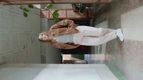 Young energetic woman, student in casual outfit, is having fun in long hallway, practicing hip-hop dancing and moving forward on camera, Vertical video, Social media concept, Slow motion.