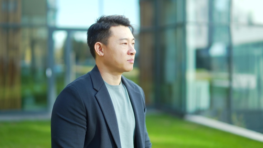 portrait handsome Asian man a university college teacher, businessman, scientist Cheerful happy educator. Standing background modern office center or campus. Outside, outdoors looking at camera. Smile Royalty-Free Stock Footage #1082493214