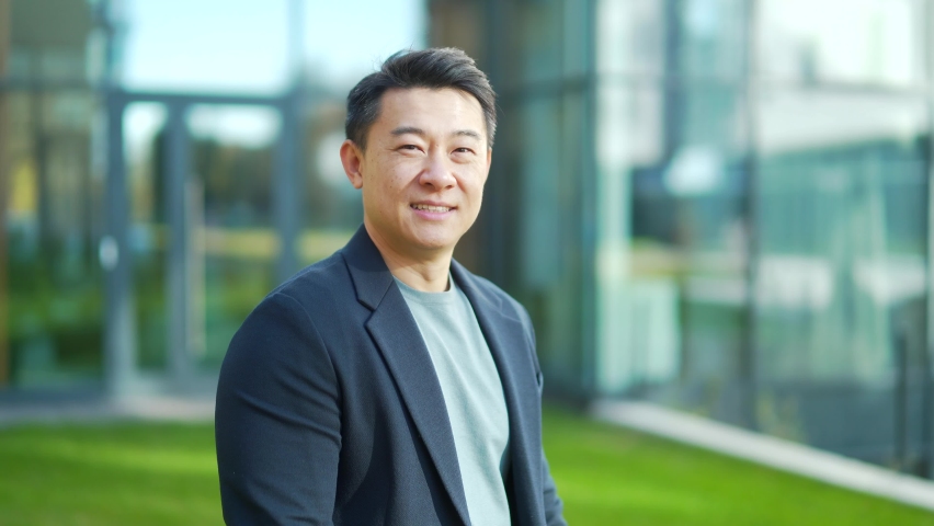 Portrait handsome Asian man a university college teacher, businessman, scientist Cheerful happy educator. Standing background modern office center or campus. Outside, outdoors looking at camera. Smile | Shutterstock HD Video #1082493214