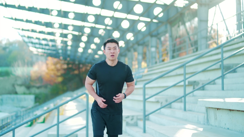 Sport asian man looking smart watch at modern track. Man runner using smartwatch bracelet. Portrait fitness man checking result. Male in sportswear jogging in the street urban background city stadium Royalty-Free Stock Footage #1082493220