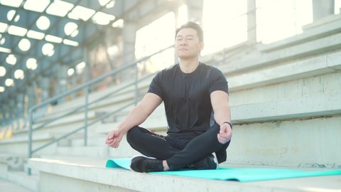 handsome asian man meditating in modern urban stadium, sitting lotus pose Male practicing yoga mat, zen. relaxes outdoors in nature in the morning Concept healthy lifestyle, relax, calm, meditation