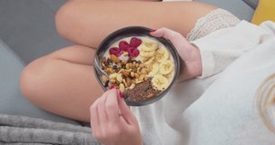 4K video of a close-up of a sportswoman eating a bowl of yogurt, raspberries, bananas, nuts and seeds for breakfast. Concepts of healthy eating, fitness and self-care.