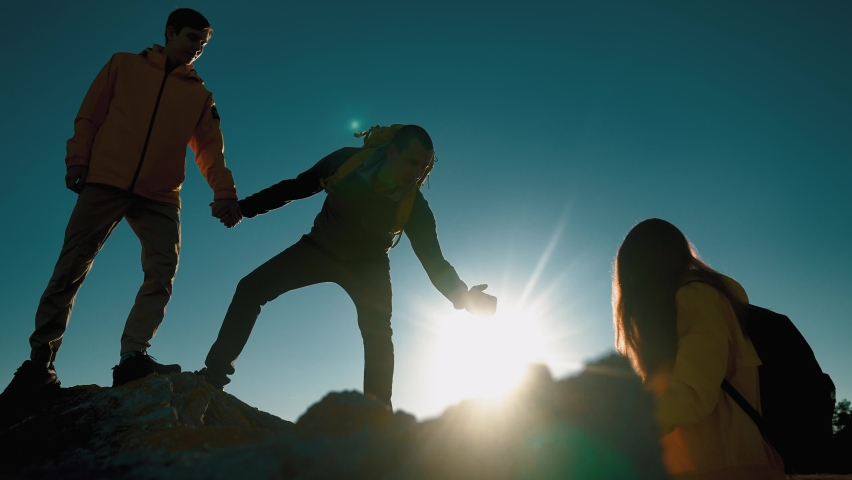 help team concept. team silhouette of climber stretching a helping hand to a friend. business teamwork success concept. silhouette business travel three tourists pull a helping sunlight hand Royalty-Free Stock Footage #1082496499