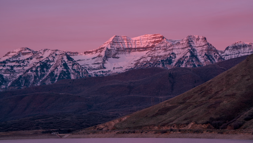 Time lapse of the sun lighting up the snow capped mountain at sunrise viewing Timpanogos Mountain from Deer Creek Reservoir in Utah.