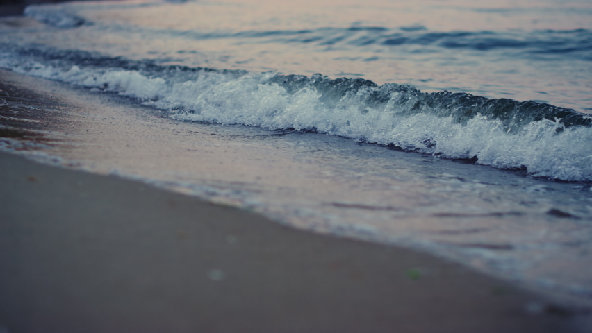 Close up blue cold ocean waves breaking sandy beach in morning dawn. Closeup water waves splashing sand seashore island in evening dusk. Meditative scenic view of coastline. Travel summer season