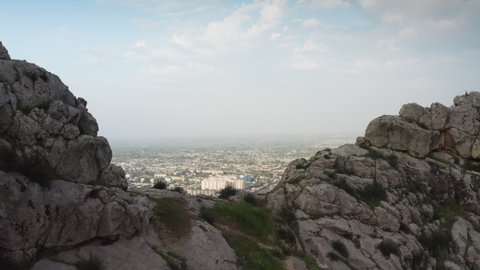 An aerial shot of a flight through a large gray stone cliff for which a wonderful cityscape of a Central Asian city opens. Urban landscape, a city at the foot of a mountain. daytime, 4k drone