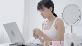 Beauty of young asian woman with learning makeup with lipstick on mouth watching laptop computer with tutorial course online, female teaching and explain make up with cosmetic on streaming media.