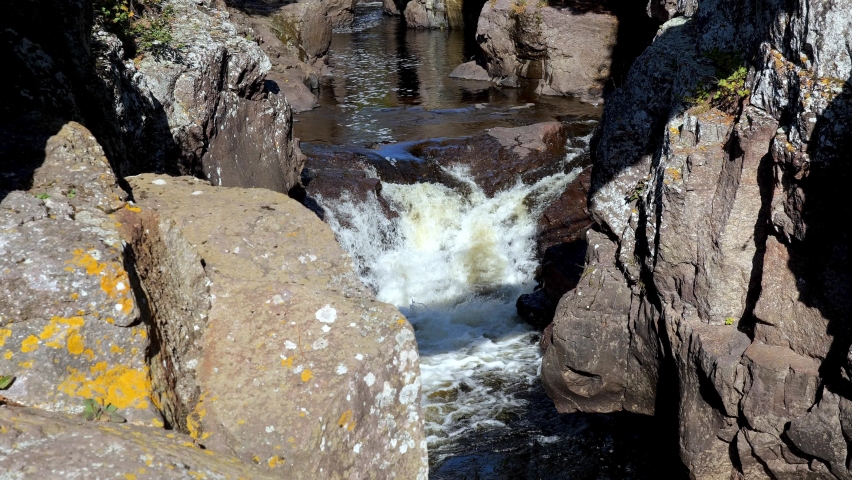 Waterfalls between rocks on the Temperance River at north shore of Lake Superior in northern Minnesota. Slow motion nature clip of cascade under pedestrian bridge, visible as shadow on white water.