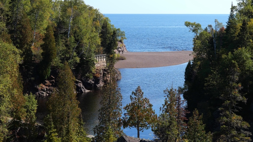 Sandbar at the mouth of the Baptism River where it enters Lake Superior in Minnesota, and a couple people walking on it. At Tettegouche State Park on the north shore of one of the Great Lakes.