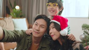 Christmas,Happy Holiday concept.three generation happy asian family sitting on floor taking selfie or video conference by mobile phone,wear Santa cap decorating Christmas tree in living room at home