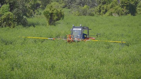 Wide shot of a worker spraying pesticides or fertilizers with the help of boom sprayer vehicle or similar  agriculture machine in a farming green field of South Asian region 