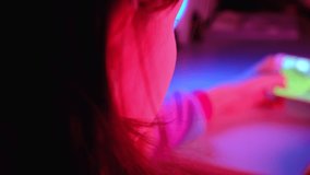 Closeup portrait of pretty young girl playing online mobile game on a smart phone. Teen girl play the game on cellphone. Gamer playing online game on smartphone in dark room. Neon blue and pink light.