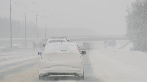 Heavy snowfall, snow-covered cars driving on highway during intense blizzard. Moscow, Russia - February 12, 2021.
