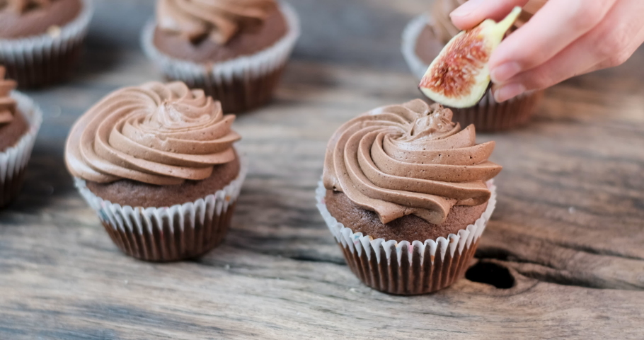Chocolate muffins on table. Cook decorates cake quarter of figs. Cup caps with whipped chocolate cream