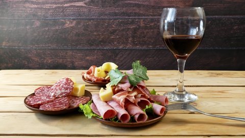 Red wine in glass and cold smoked meat plate, antipasto set platter wooden plate. Wine and cold smoked meat plate with sliced ham, prosciutto, bacon. Copy space. Top view