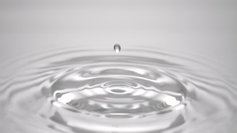 Macro shot of water drop falls down on grey transparent fluid surface creating water rings on it on light grey background | Abstract skin moisturizing cosmetics formulation concept