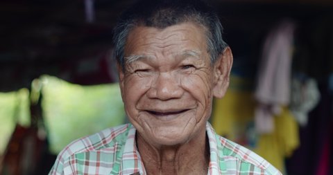 An Asian man who is more than seventy years old and works as a wage earner in a farm, live in a poor house, smiling and laughing happily.