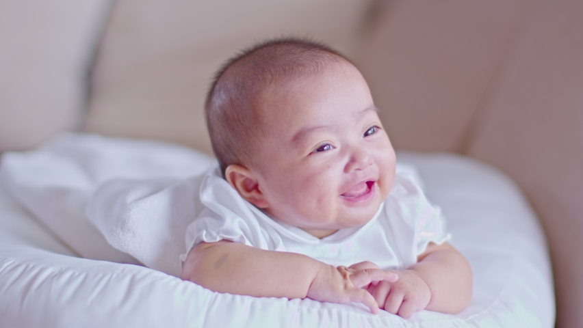 Adorable Asian baby girl lying on bed looking at camera.Cute little baby smiling and happiness relaxing in bed.Portrait of asian baby newborn in bedroom,Soft focus