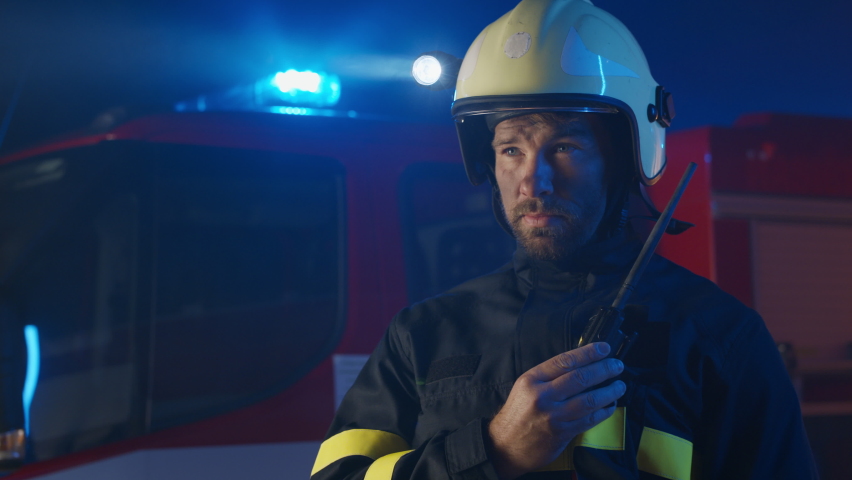 Mid adult firefighter man talking to walkie talkie with fire truck in background at night. Royalty-Free Stock Footage #1082523991