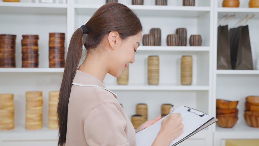 Portrait of Asian beautiful woman selling vase product online at home. Young attractive girl stand with confidence checking goods in warehouse store for customer then cross arm and looking at camera.