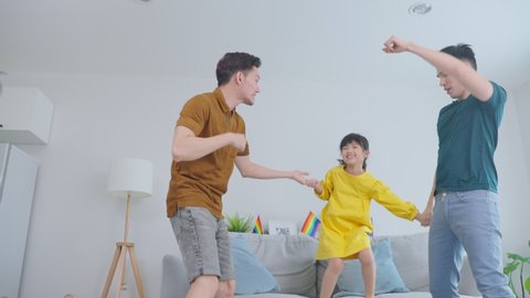 Asian handsome man gay family dance together with young kid daughter. Attractive romantic male lgbt couple spend time and enjoy listen to music, have fun with little girl child in living room at home.