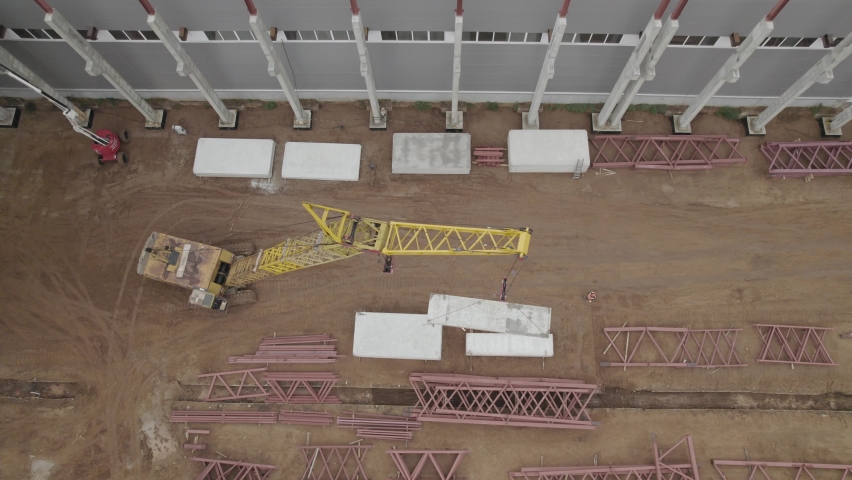 Aerial view. A heavy crane at a construction site is lifting iron concrete slabs.
