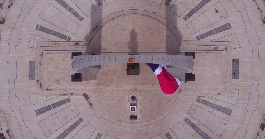 Flag waving in the wind under monument sculpture in Plaza de la Bandera, Santo Domingo. Aerial top-down rising