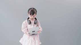 Child with headset watching videos with digital tablet. Gray Background with Copy Space.