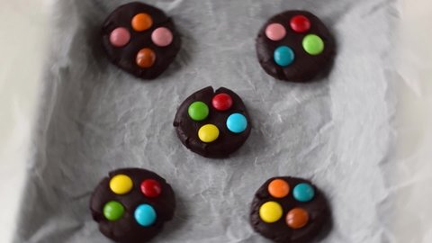 Making chocolate cookies with multicolored candy drops. Shaped raw pastry dough on the baking sheet is rotating. Cooking desserts at home. Zoom out
