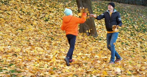 Young Boy Son and Father Having Fun at Autumn Park. Cheerful Child Throwing Yellow Leaves with Happy Mood Outdoors. Portrait of Happy Family Playing with Foliage in Autumn Weather