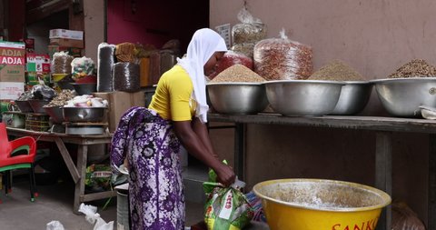 NIMA, GHANA - 30 OCT 2021: Muslim woman seed grain market Accra Ghana part 1. Urban market stall along busy poor neighborhood street. Day to day living poor economy.