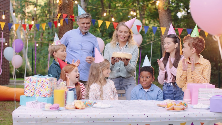 Happy children in party hats with party blowers at the birthday party applauding and having fun while mother bringing a cake Royalty-Free Stock Footage #1082534299
